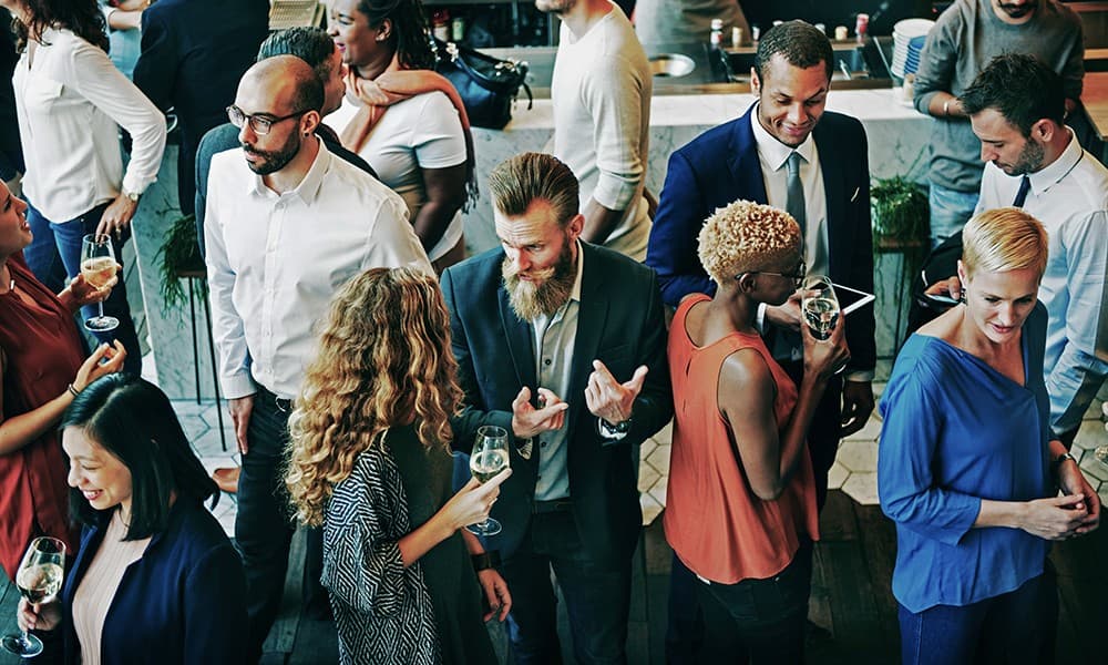 A crowded reception of well-dressed professionals mingling, talking, and holding wine glasses.