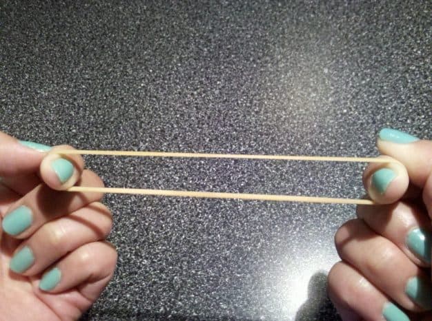 Two hands stretching a rubber band taut against a dark surface, representing the tension of setting and reaching a stretch score target.