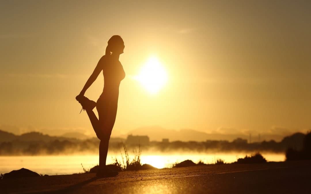 Silhouette of a runner stretching at sunrise beside a misty lake, illustrating the independence and self-direction of student life.