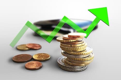 A stack of coins beside a rising green arrow graph, symbolizing cost of attendance and financial planning.
