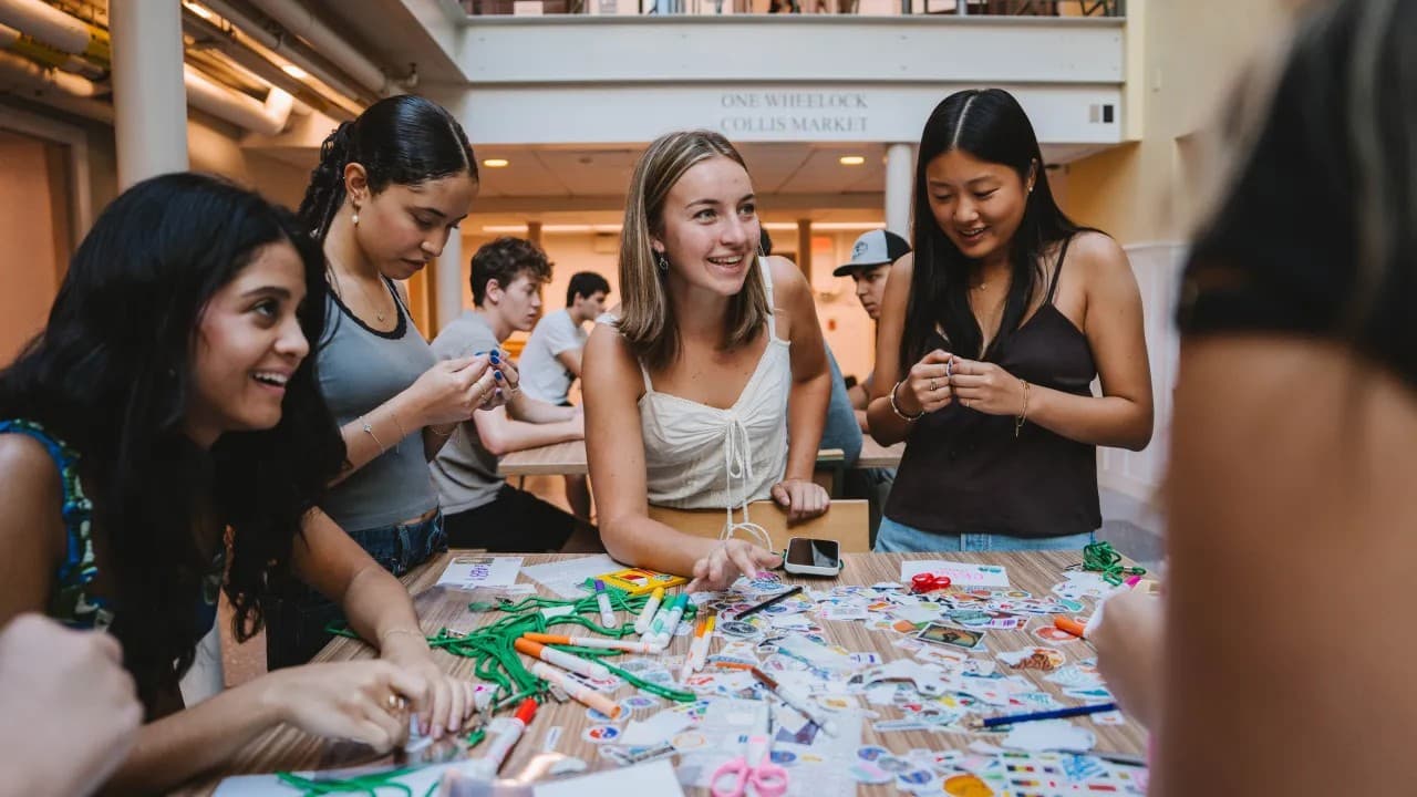 A group of Dartmouth students smiling and making friendship bracelets together at a table inside the Class of 1953 Commons.