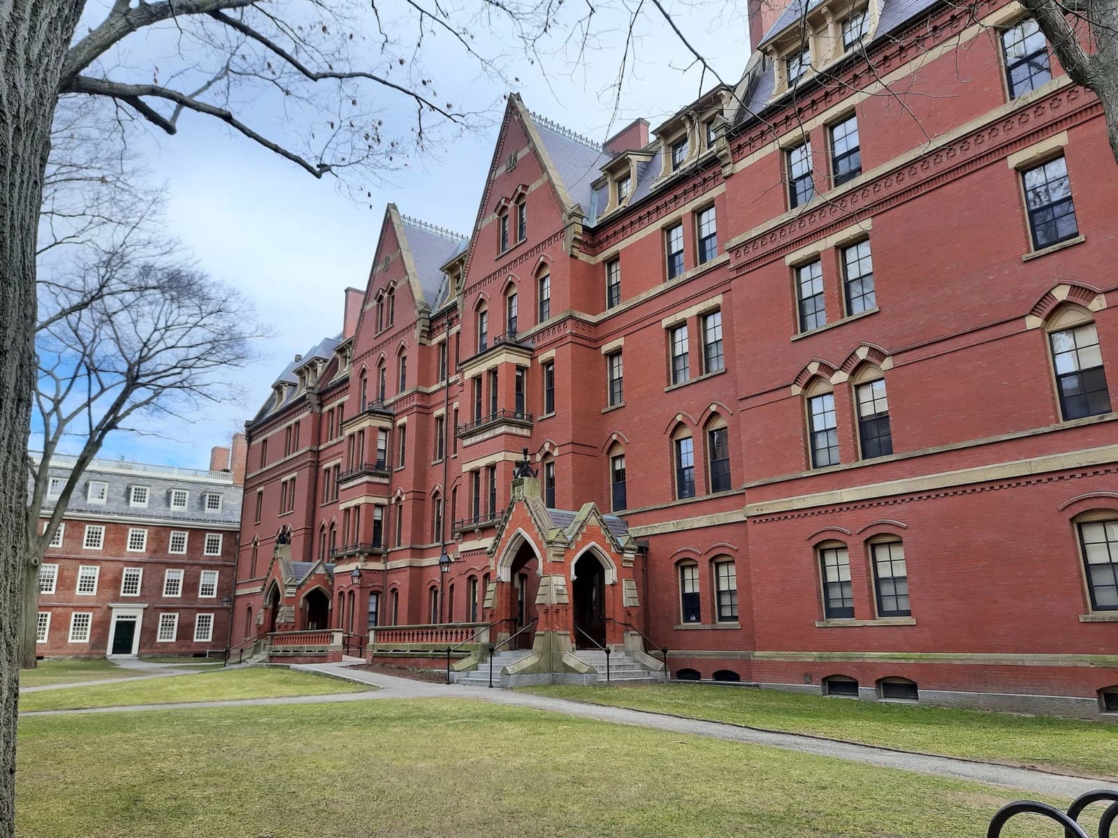 A red-brick Harvard Yard dormitory with steep gabled roofs and Gothic archway entrances, framed by bare winter trees.