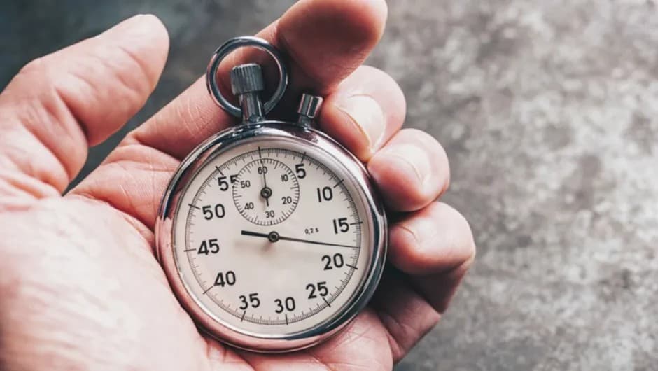 A close-up of a hand holding a stopwatch with its dial and hands visible.