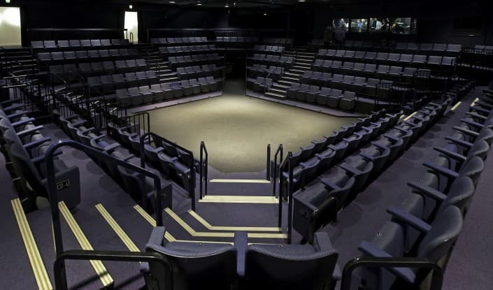 An empty tiered theater seating area viewed from the back, arranged in a wedge shape around a center aisle.
