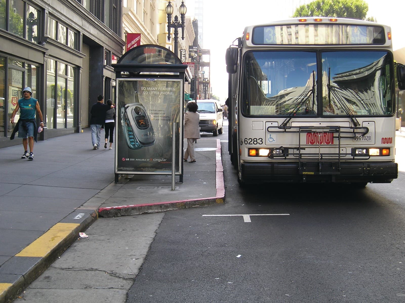 A city bus stopped beside a bus shelter on a busy sidewalk lined with pedestrians and storefronts.